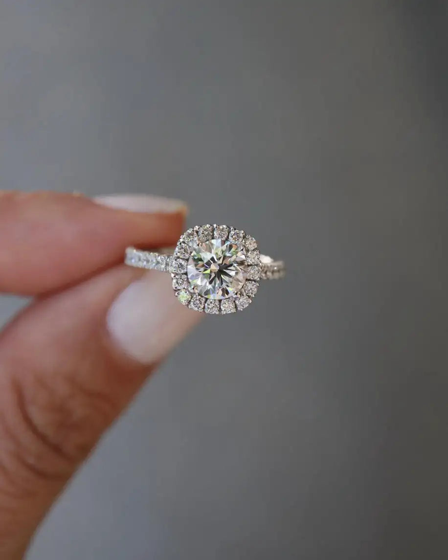 Diamond ring held by a hand against a neutral background